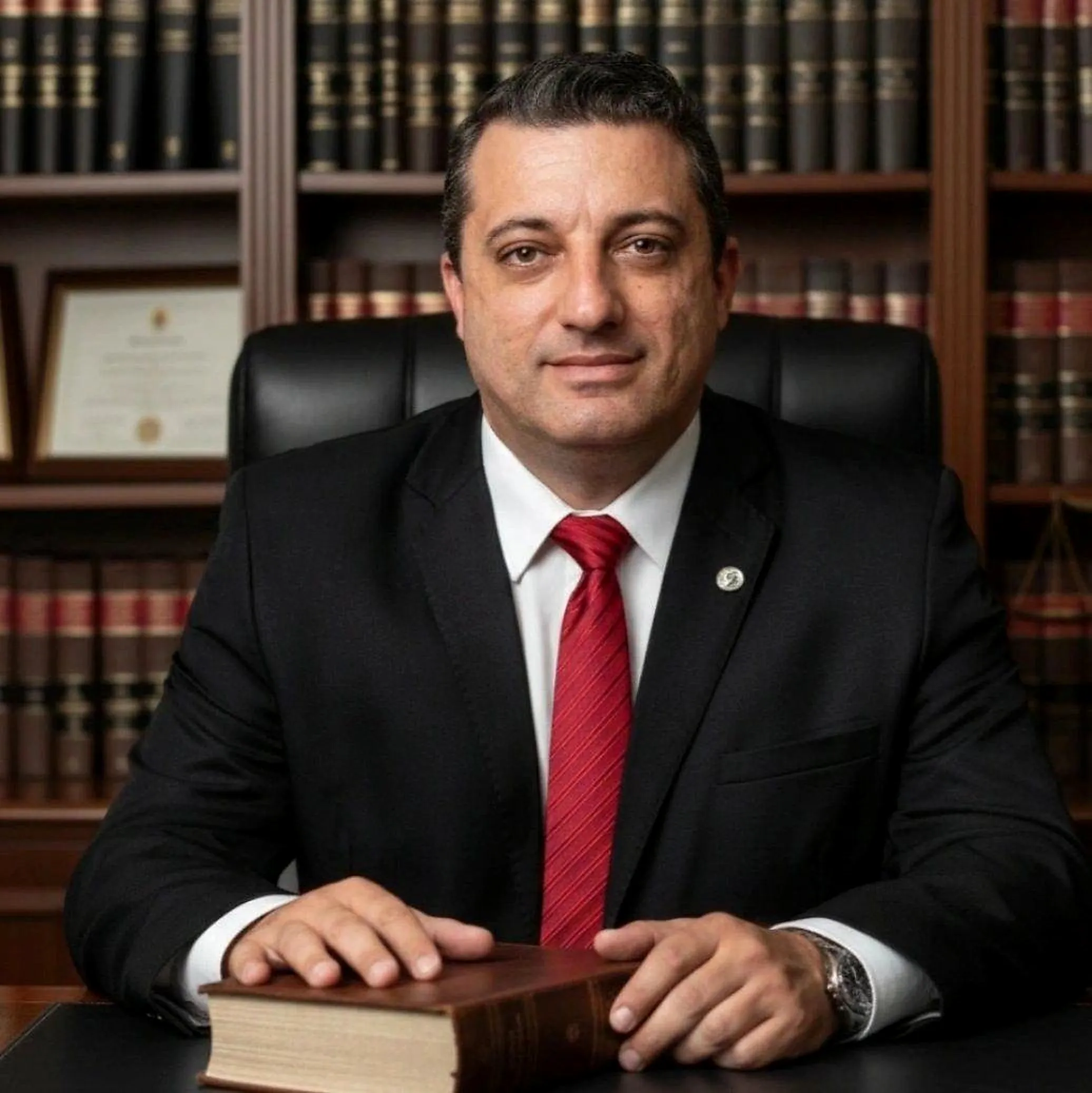 Dr. Maicon Nunes Santos em seu escritório, com estante de livros jurídicos ao fundo